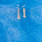 Feet dangling inside a pool with blue tiles