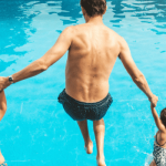 A father and two kids jumping into a swimming pool.
