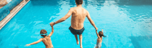 A father and two kids jumping into a swimming pool.