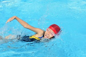 young girl with goggles and swimming cap doing a lap race