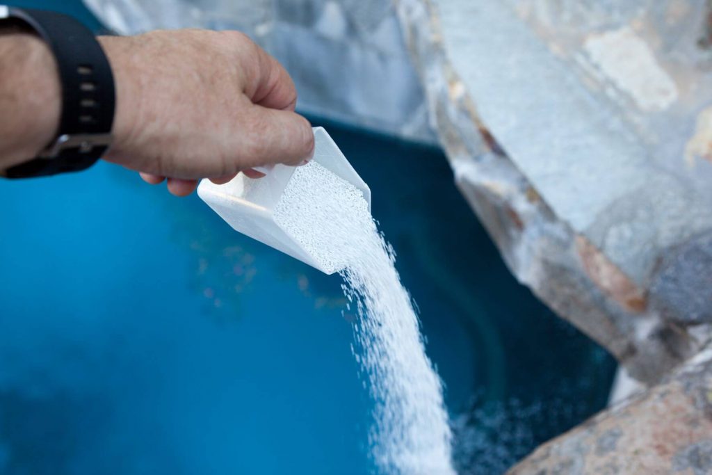 A hand pouring pool shock into a pool