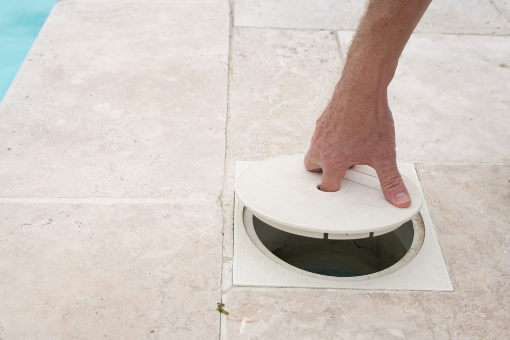 A person removing the filter cover on a pool deck