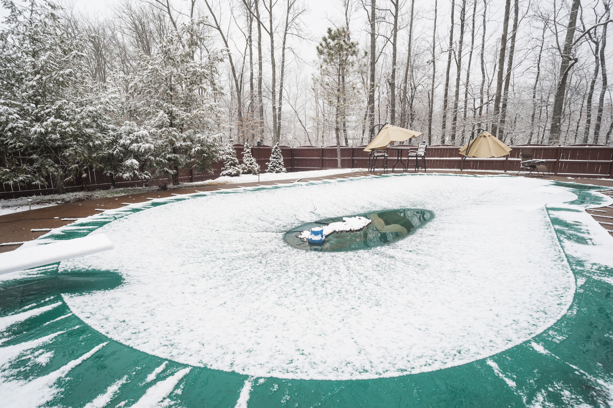 Inground swimming pool with cover on it and water pump during a snowfall in winter, Indiana, USA