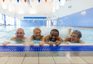 4 seniors holding on to the edge of a large pool and smiling.