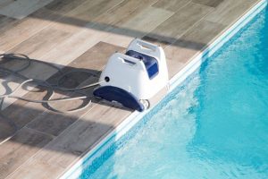 A photo of a robot pool cleaner on a deck next to a pool.